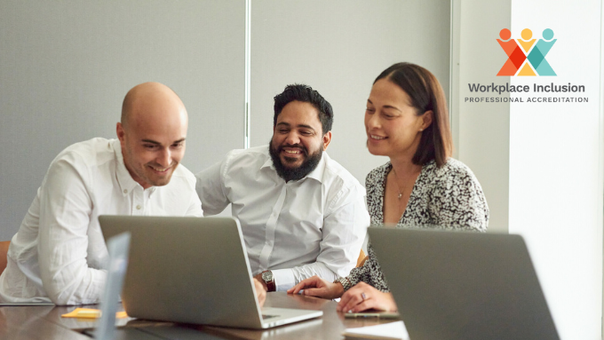 Two men and one woman sitting at an office table looking at two laptops