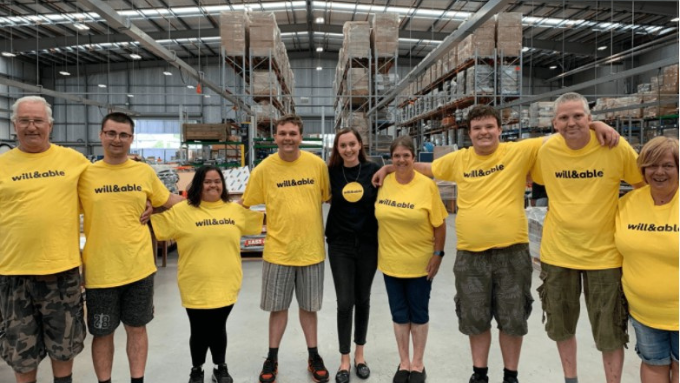 Will&Able group photo inside a warehouse everyone smiling at the camera with the same t-shirt on