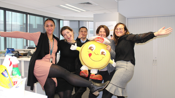 five people posing for a group photo indoors with a plush toy 
