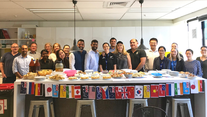 team in a lunch room with a table full of food everyone behind the table and smiling at the camera
