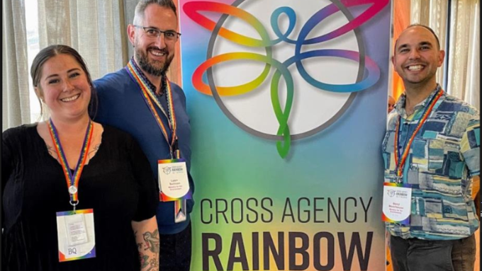 three people standing in front of a rainbow sign indoors
