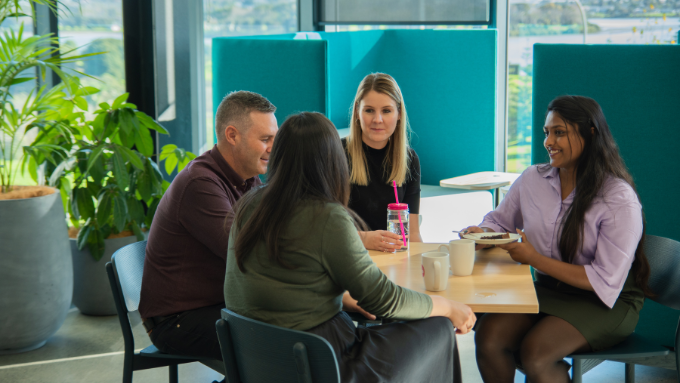 four workers having a conversation between each other all seated at a table indoors