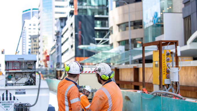 Two men wearing hard hats on work site, backs to camera.