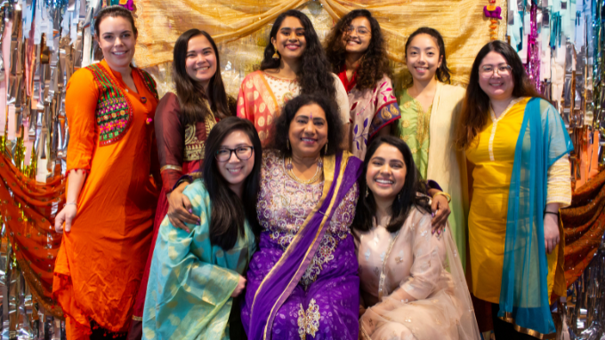 women group photo all smiling at the camera with decorations behind them and all in traditional clothing 
