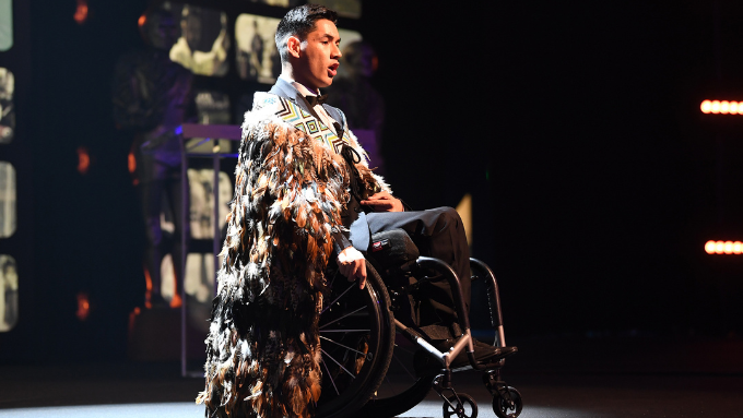 male on stage in a wheel chair speaking 