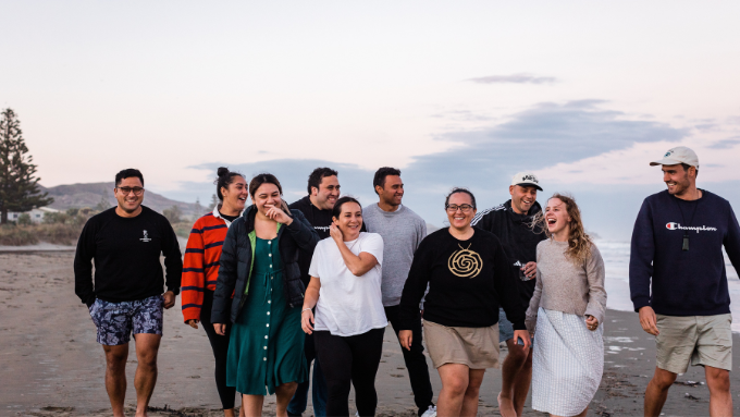 A group of ten young KPMG staff walking on a beach smiling and laughing