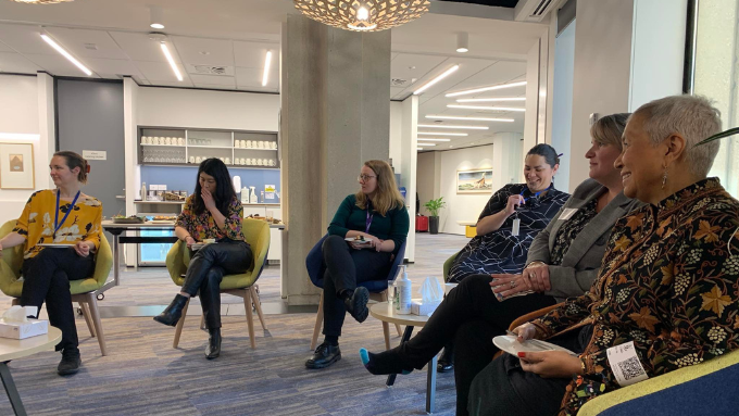 six women all seated in a circle in a meeting room six women all seated in a circle in a meeting room