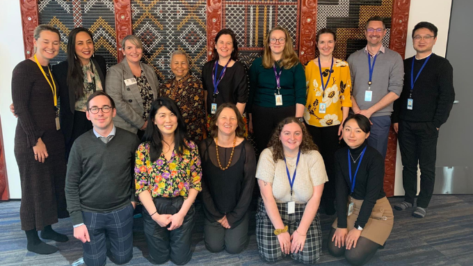 The Treasury group photo all smiling looking at the camera with a maori design behind them