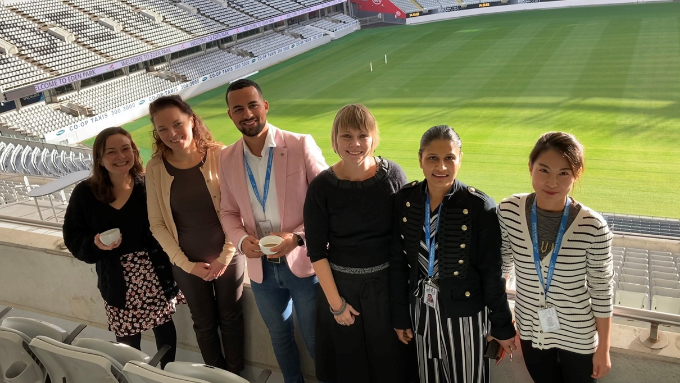 Some of the Belong Aotearoa team standing at the top of a rugby stadium with the field in the background