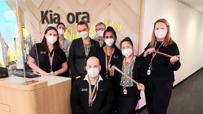 A group of ASB Bank staff by a bank tellers desk wearing covid masks and rainbow lanyards