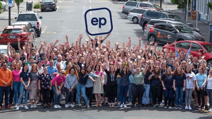 a large group of people standing in the middle of a road all looking and waving at the camera and one person is holding up a sign with the letters EP a large group of people standing in the middle of a road all looking and waving at the camera and one person is holding up a sign with the letters EP