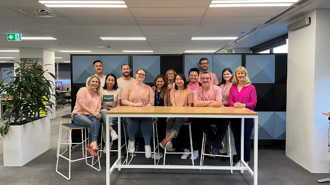 a team all dressed in pink sitting at a table facing and smiling at the camera