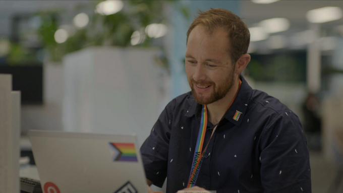 A man wearing a rainbow lanyard looking at his laptop
