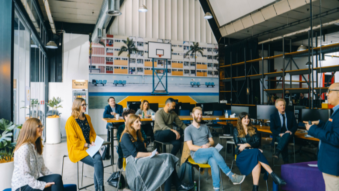 Yellow meeting room with everyone seated indoors and looking at the main speaker 