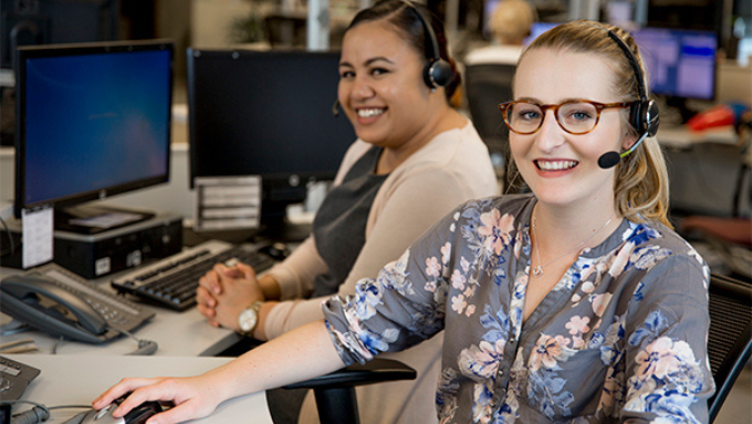two women smiling at the camera both with chat headsets on