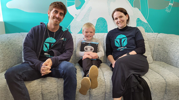 two lawvu workers and a child sitting on a couch smiling at the camera after gifting the child a book