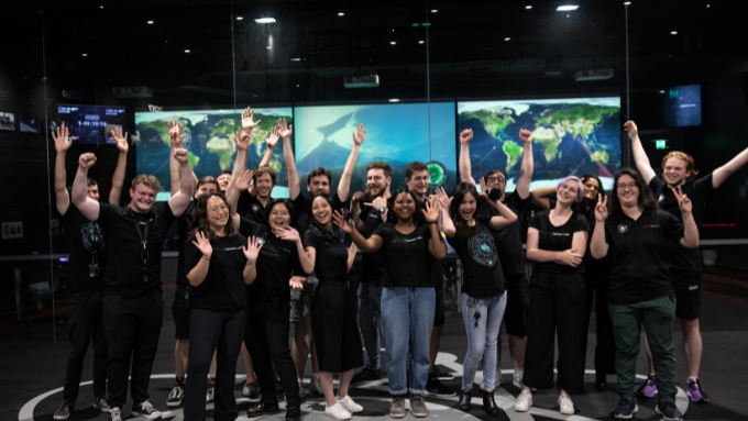 group photo of a team cheering and smiling in front of four tv screens showing the earth and space