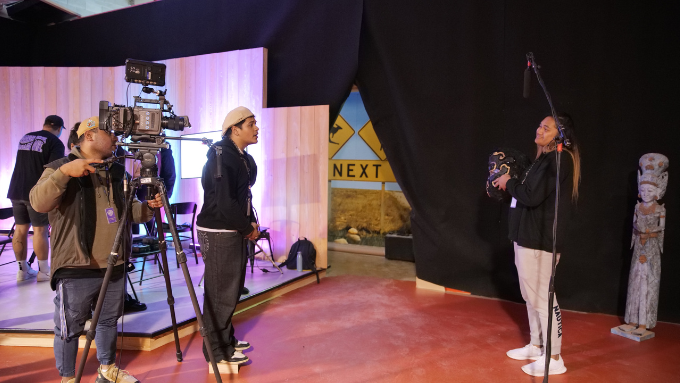Man operating camera and another man in front of woman being filmed