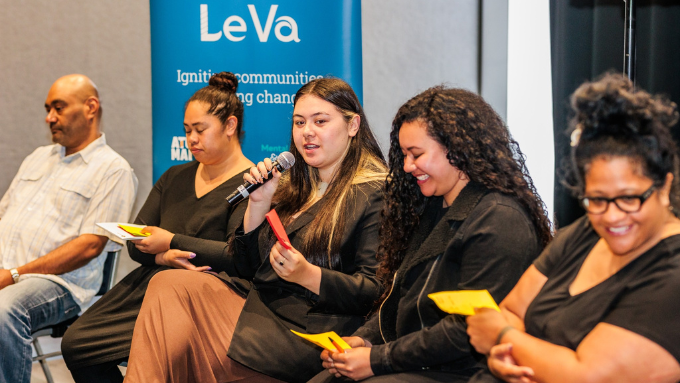 Le Va group sitting down indoors with one lady talking into a microphone 