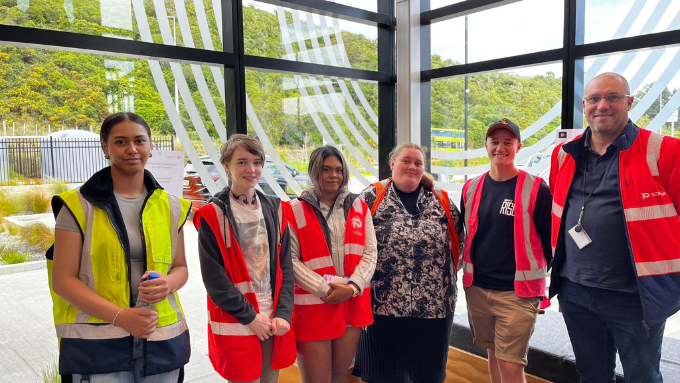group photo of six people wearing HIVIS vests looking and smiling at the camera indoors