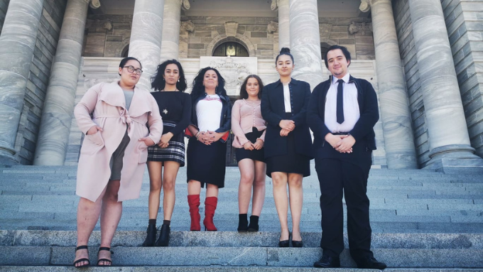 five women and one male standing on the stairs of a big building looking towards the camera 