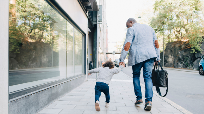 A father holding hands with his child walking down a footpath with their backs to the camera