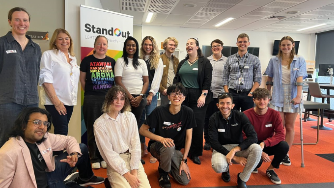 stand out group photo all looking and smiling at the camera indoors with the team logo behind them stand out group photo all looking and smiling at the camera indoors with the team logo behind them