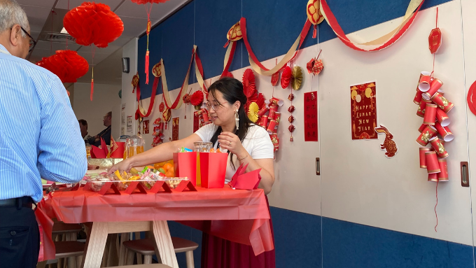 a women standing behind a table of colourful food and drinks serving guests for Chinese New Year with decorations on the wall a women standing behind a table of colourful food and drinks serving guests for Chinese New Year with decorations on the wall