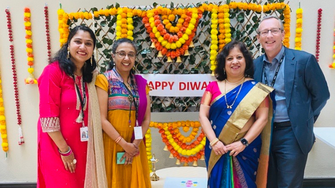 Ministry of Business Innovation employees smiling, with three women in traditional dress, celebrating diwali against a colourful background