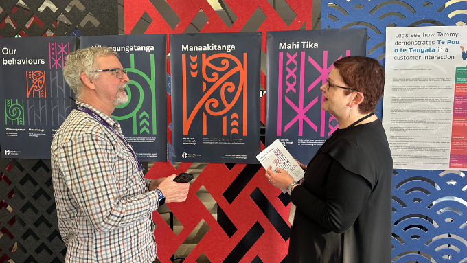 two people talking to each other in front of māori designs indoors
