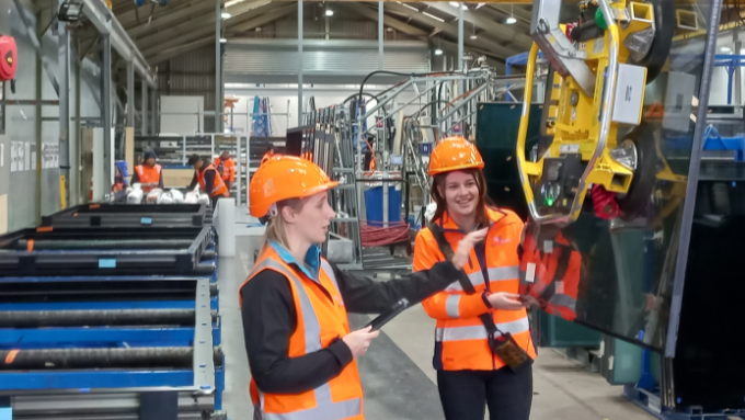 two women factory workers using a machine picking up glass