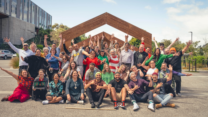 big group of people standing infront of a marae entrance all smiling at the camera 