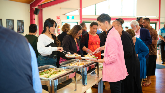 A group of people serving food at a buffet at a marae for an event for Auckland University of Technology