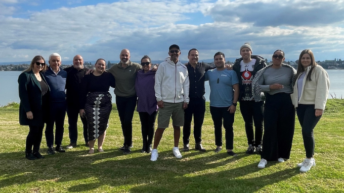 Twelve people from KPMG standing on a hill with water in front of lake smiling Twelve people from KPMG standing on a hill with water in front of lake smiling