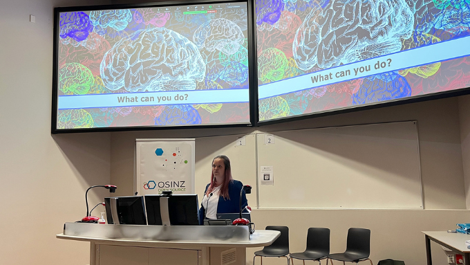 A teacher presenting about neuroscience from a lectern with an image of a brain on a big screen behind them A teacher presenting about neuroscience from a lectern with an image of a brain on a big screen behind them