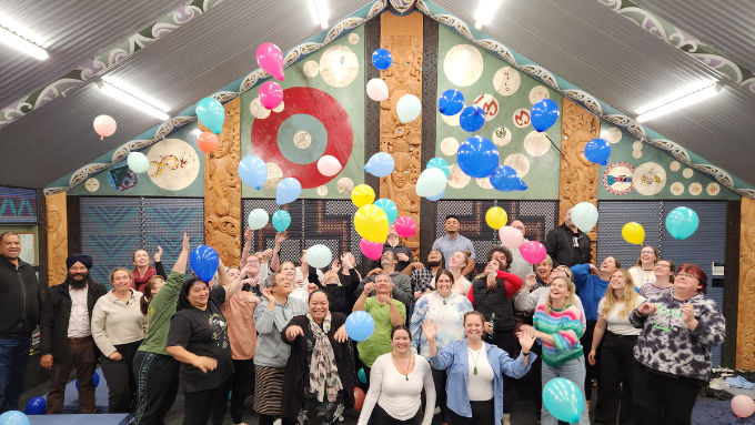A group of Ara Poutama Aotearoa Department of Corrections staff celebrating inside a marae with colourful balloons
