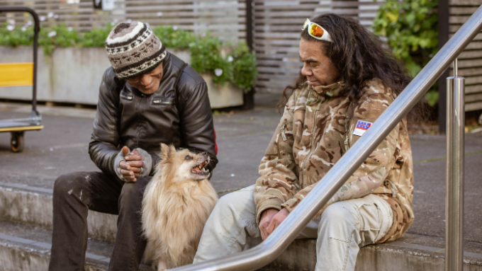 Two males sitting on some outdoor steps talking with a Pomeranian dog