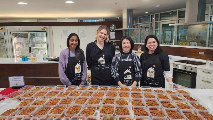 Four DUAL staff standing in front of a large table of prepared meals they have prepared to be sent out to children in need Four DUAL staff standing in front of a large table of prepared meals they have prepared to be sent out to children in need