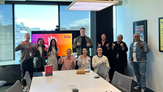 NZ lotto commission group photo with everyone holding thumbs up in a meeting room with the window and a tv in the background NZ lotto commission group photo with everyone holding thumbs up in a meeting room with the window and a tv in the background
