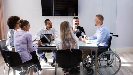 Man in wheelchair at head of boardroom table talking to colleagues seated around table Man in wheelchair at head of boardroom table talking to colleagues seated around table